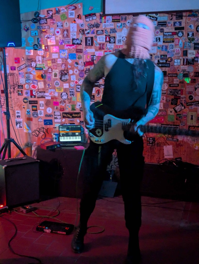 bassist wearing an orange balaclava and hardcore black pants